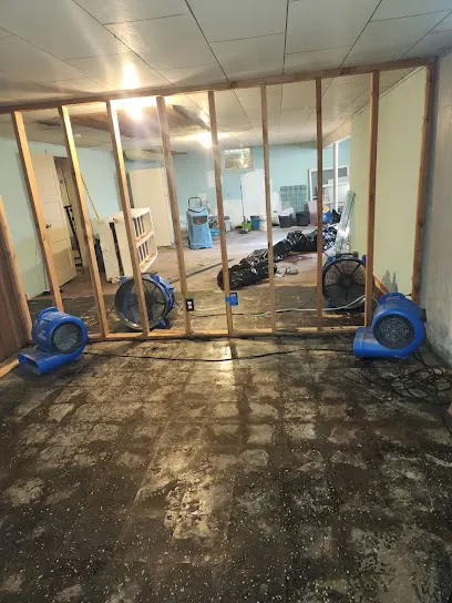 Air movers drying a wet floor behind exposed wall framing in Weld County